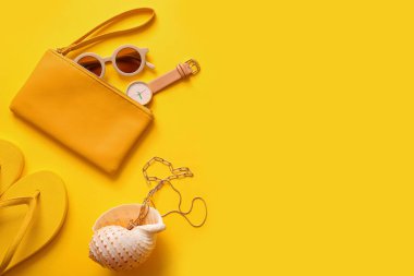 Saati olan şık bir çanta ve sarı arka planda farklı aksesuarlar.