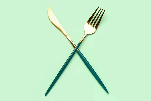 緑の背景にステンレス製のフォークとナイフ — ストック写真
