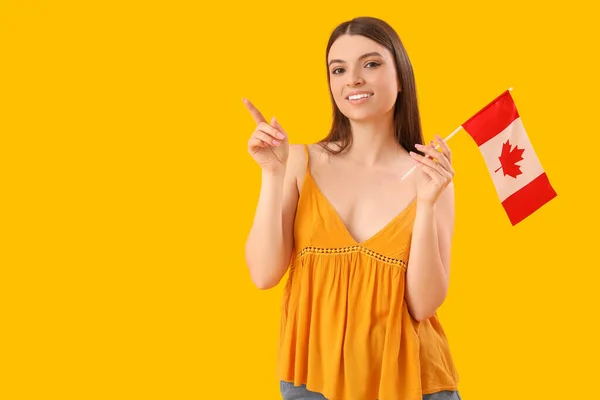 拿着加拿大国旗指着黄色背景的东西的年轻女子 — 图库照片