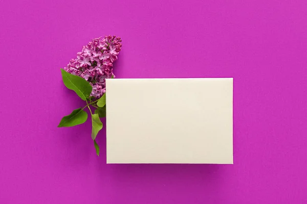 Blank card and lilac flowers on purple background