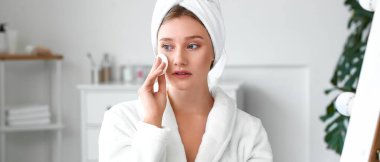 Güzel genç bir kadın banyoda makyajı temizliyor.