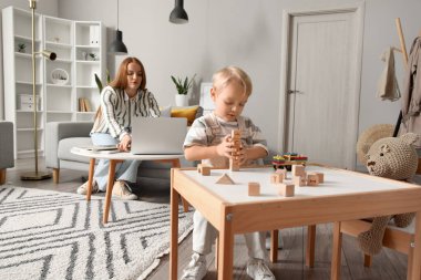 Annesi evde çalışırken küçük sevimli çocuk tahta oyuncaklarla oynuyor.