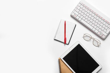 Beyaz arkaplanda tablet bilgisayar, defter, klavye ve gözlük ile kompozisyon