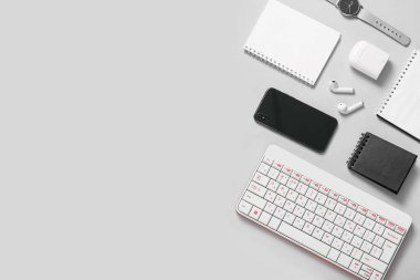 Beyaz arkaplanda cep telefonu, klavye, kulaklık ve defter kompozisyonu