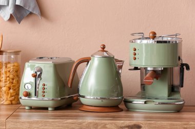 Elektrikli çaydanlık, kahve makinesi ve bej duvarın yanındaki ahşap mutfak tezgahında ekmek kızartma makinesi.