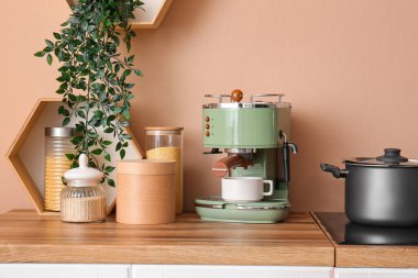 Bej duvarın yanındaki ahşap mutfak tezgahında fincanı olan modern kahve makinesi.