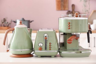 Elektrik ısıtıcısı, tost makinesi ve kahve makinesi mutfaktaki beyaz masada.