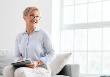 Not defteriyle ofiste oturan olgun bir psikolog.