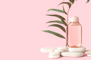 Bitki dalı ve pembe arka planda spa taşları olan bir şişe mikiler suyu.