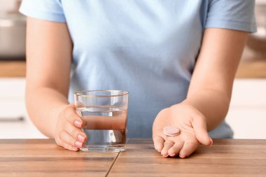 Ahşap masada bir bardak su ve coşkulu tablet tutan bir kadın.