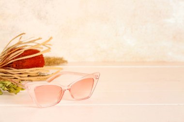 Beyaz ahşap masada kurumuş çiçekli şık güneş gözlükleri, yakın plan.