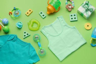 Açık yeşil arka planda bebek kıyafetleri ve aksesuarları olan kompozisyon