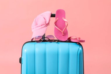 Pembe arka planda plaj aksesuarları olan bavul.