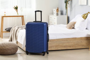 Mavi bavul yatağın yanında, aydınlık odada.