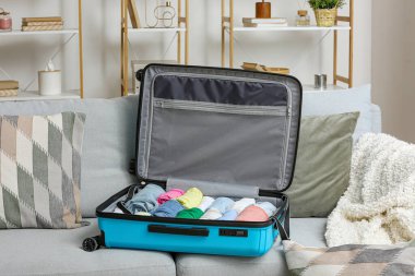 Oturma odasındaki kanepede katlanmış giysilerle bavulu aç.