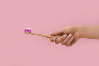 Pembe arka planda diş fırçası ve yapıştırıcısı olan bir kadın eli.