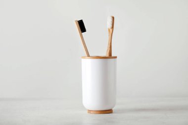 Beyaz masanın üzerinde bambu diş fırçası olan tutucu.