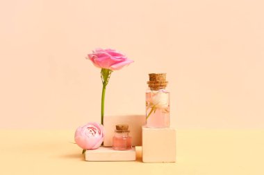 Gül özlü kozmetik yağı şişeleri ve bej arka planda çiçekler