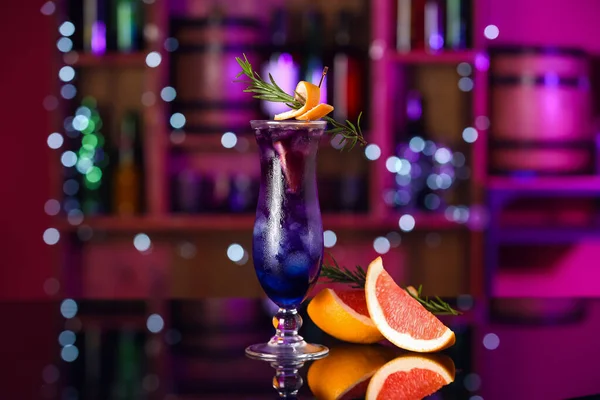 stock image Glass of purple gin and tonic with grapefruit and rosemary on table in bar against blurred background