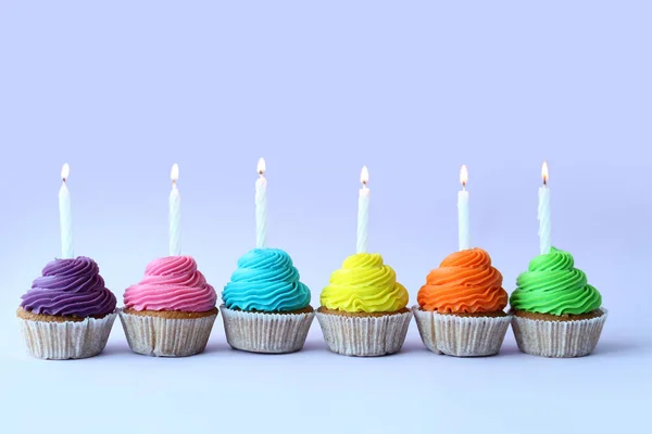 Tasty cupcakes with birthday candles on blue background