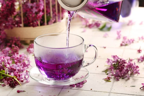 Pouring Hot Lilac Tea Glass Cup Flowers Light Tile Table — Stock Photo, Image