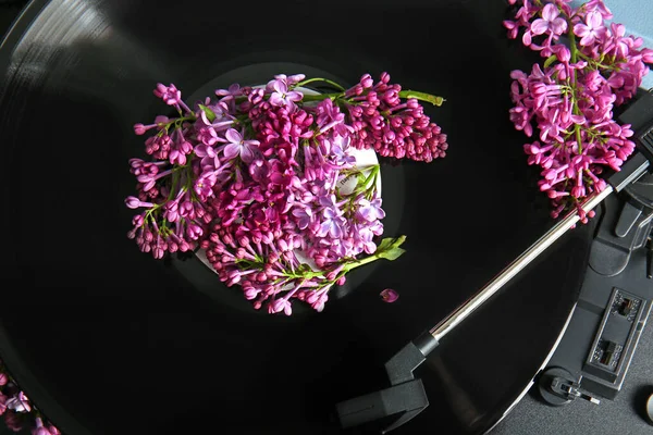 Record player with vinyl disk and beautiful lilac flowers, closeup
