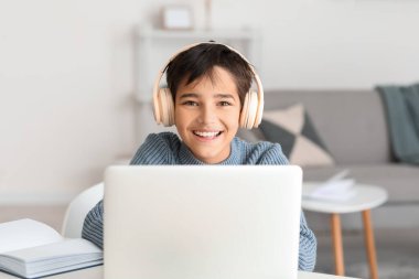 Happy little boy in headphones using laptop at home