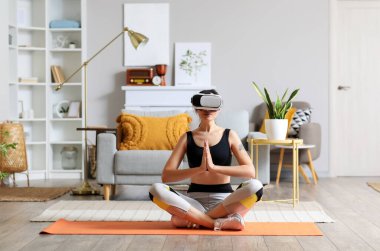 VR gözlüklü genç bir kadın evde meditasyon yapıyor.