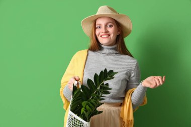 Yeşil arka planda ip torbasında saksısı olan genç bir kadın.