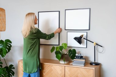 Olgun bir kadın evdeki ışık duvarına boş bir çerçeve asıyor.