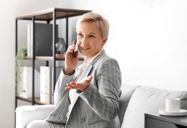 Ofisteki koltukta otururken telefonla konuşan olgun bir iş kadını.