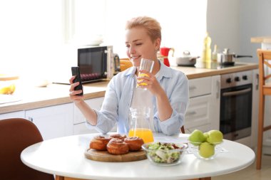 Mutfakta cep telefonu ve bir bardak meyve suyu olan genç bir kadın.
