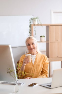 Ofiste çalışan olgun bir kadın programcı ve bir fincan kahve.