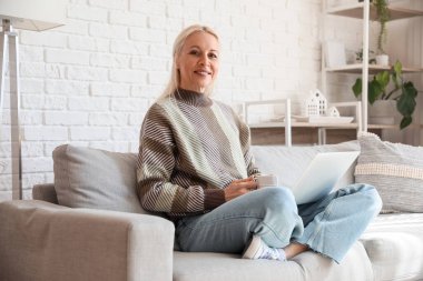 Evde çalışan bir fincan kahve ve dizüstü bilgisayarı olan olgun bir programcı.