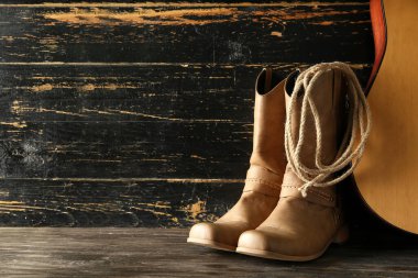 Kovboy çizmeleri, gitar ve kementle tahta arka planda