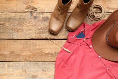 Kovboy çizmeleri, şapka ve kırmızı gömlek ahşap arka planda.