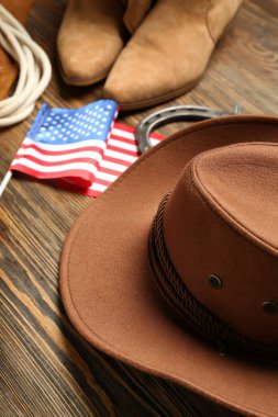 Farklı kovboy aksesuarları ve kahverengi ahşap arka planda Amerikan bayrağı olan kompozisyon
