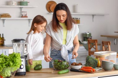 Annesi mutfakta sağlıklı salata pişiren küçük bir kız.