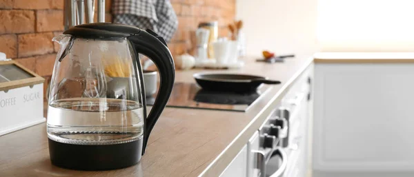 Modern electric kettle with water on counter in kitchen