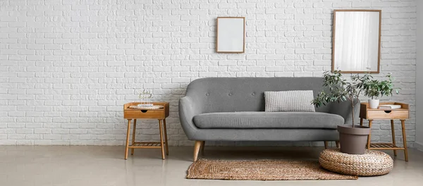 房间里靠近白色砖墙的灰色沙发 上面有桌子和室内植物 设计横幅 — 图库照片