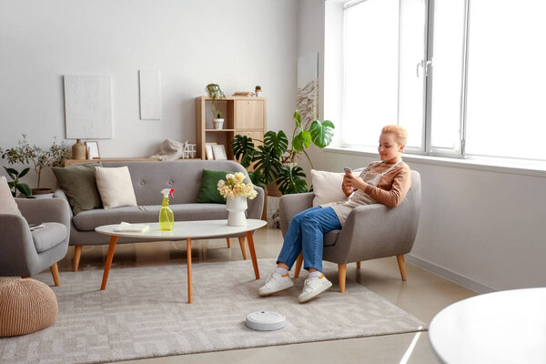 Молодая женщина с помощью мобильного телефона во время уборки дома