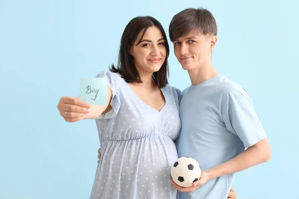 年轻的怀孕夫妇拿着印有Boy字样的纸 蓝色背景的球 — 图库照片