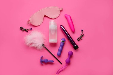 Bir şişe kayganlaştırıcı ve pembe arka planda seks oyuncakları