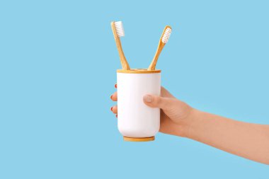 Mavi arka planda bambu diş fırçası tutan kadın eli.