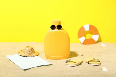 Güneş gözlüklü güneş kremi şişesiyle yaratıcı kompozisyon ve kumdaki plaj aksesuarları.