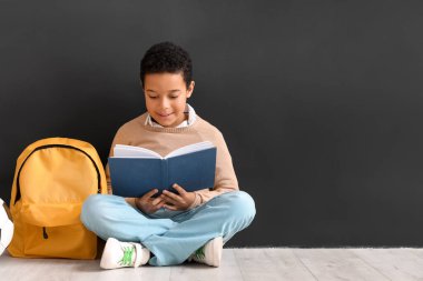 Kara tahtanın yanında kitap okuyan küçük Afro-Amerikalı çocuk. Çocuk Bayramı kutlaması