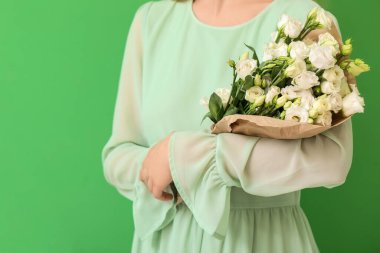 Yeşil arka planda güzel Eustoma çiçekleriyle dolu buketi olan genç bir kadın.