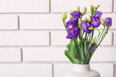 Beyaz tuğla arka planda Eustoma çiçekleri olan vazo
