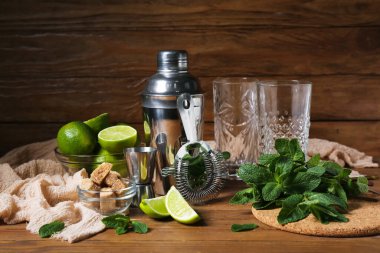Ahşap zemin üzerinde mojito hazırlamak için gözlük, karıştırıcı, süzgeç ve malzemeler.