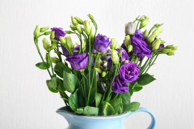 Beyaz arka planda Eustoma çiçekleri olan sürahi.